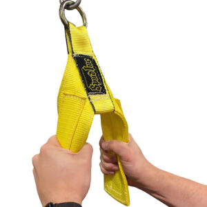 A person holding the Spud Inc Track Harness, a bright yellow nylon lifting sling featuring reinforced stitching and a metal ring at the top for hook attachment.