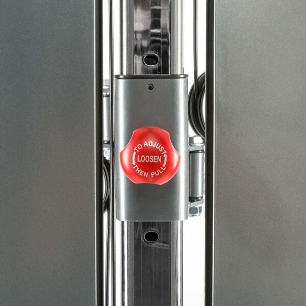 Close-up of a metal adjustment mechanism with a red knob labeled To Adjust Loosen Then Pull. The mechanism is part of a polished metal frame, possibly from a wall mounted cable machine or similar exercise equipment.