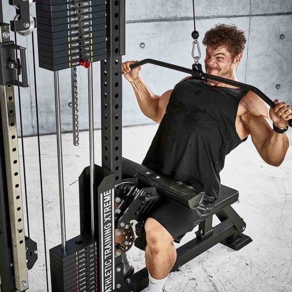 A man in a black tank top works out on a cable machine at a modern gym, pulling an ATX® Lat Bar Blackline down to his chest while seated on a padded bench, surrounded by gym equipment and weight stacks.