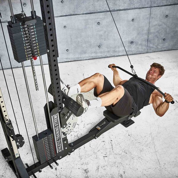 A man in athletic gear is using an ATX® Lat Bar Blackline on a rowing machine against a textured concrete wall, creating an industrial look. The machine includes weights and cables for a full workout.