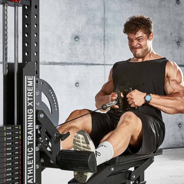 A person wearing a black tank top, dark shorts, white socks, and athletic shoes is focused while using the ATX® Cable Row Handle Blackline on a rowing machine in front of a concrete wall.