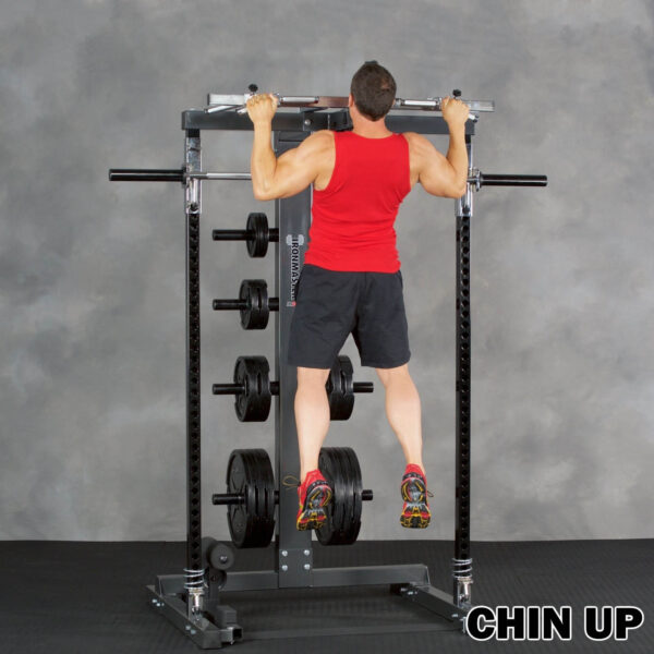 A person in a red tank top and black shorts performs a chin-up on the Ironmaster IM2000 Self-Spotting Smith Machine, with various weight plates visible. The floor is covered with black rubber matting. Text reads CHIN UP.