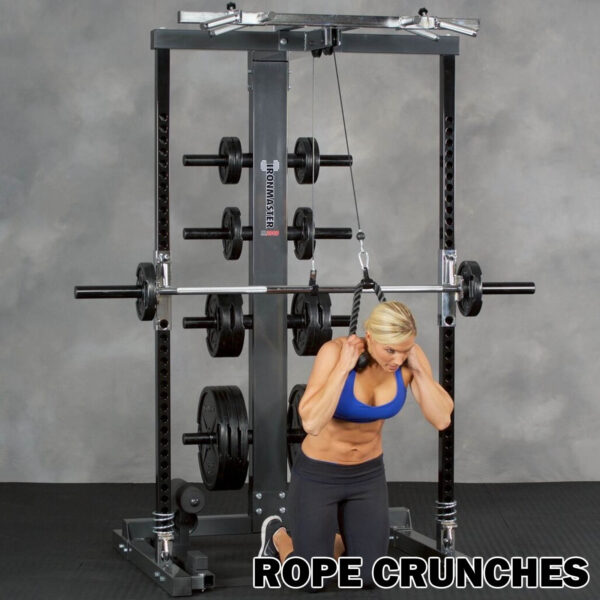 A person in athletic wear performs rope crunches on the Ironmaster IM2000 Self-Spotting Smith Machine. Kneeling, they pull a rope attachment toward their head, engaging core muscles. The machine supports multiple weight plates. The text ROPE CRUNCHES appears at the bottom.