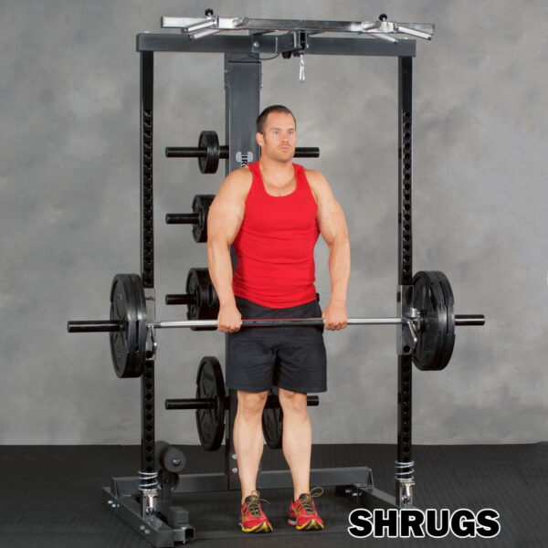 A person in a red tank top and black shorts uses the Ironmaster IM2000 Self-Spotting Smith Machine to perform shrugs in a gym, with a weight rack behind them. SHRUGS is displayed in the lower right corner.