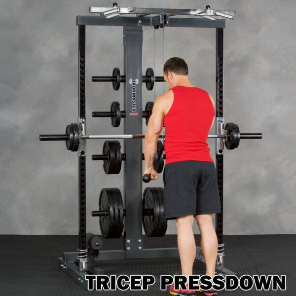 A man in a red sleeveless shirt and black shorts does a tricep pressdown on an Ironmaster IM2000 Self-Spotting Smith Machine at the gym, with TRICEP PRESSDOWN shown at the bottom.