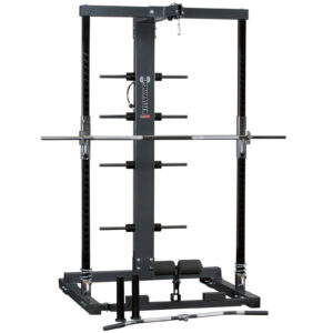 The Ironmaster IM2000 Self-Spotting Smith Machine features adjustable safety bars, a pull-up bar, and multiple weight plate holders. A barbell rests on the safety hooks, with attachments like a curl bar and handle lying before it.