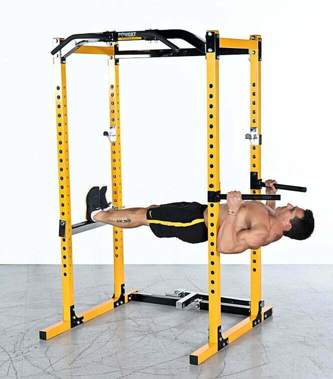 A man performs an inverted row using a bright yellow power rack in a gym setting. Hes gripping the bar with both hands, legs extended, and body parallel to the ground. The floor is gray, and the background is plain white.