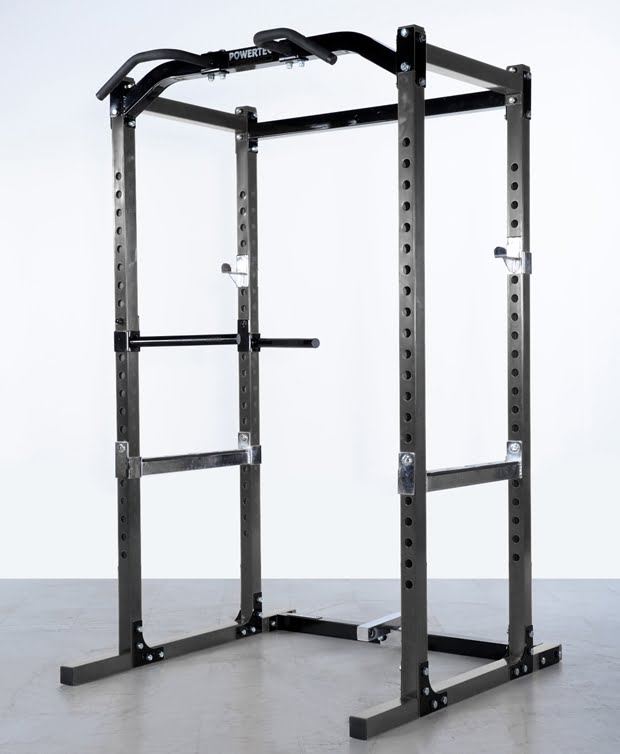 A black power rack for weightlifting standing on a gray floor. It features adjustable safety bars, a pull-up bar, and dip handles, all designed for strength training exercises.