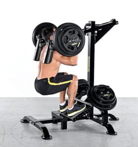 A man in a black and yellow gym outfit performs hack squats on a machine, lifting heavy weights in a fitness studio with a gray floor and white background.