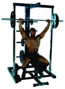 A person performs a shoulder press exercise using a barbell on a seated rack machine. The person appears focused and is in a gym setting, showcasing a weightlifting routine.