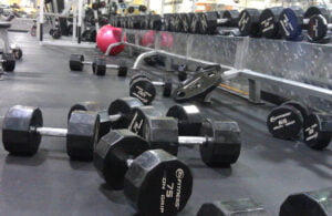 A gym floor strewn with dumbbells and weight plates, while a mirrored wall reflects the equipments gleam. An exercise ball lingers in the background, silently challenging the notion that Drop Sets Are For Posers.