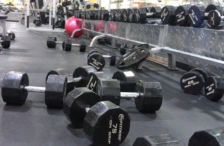 A gym floor strewn with dumbbells and weight plates, while a mirrored wall reflects the equipments gleam. An exercise ball lingers in the background, silently challenging the notion that Drop Sets Are For Posers.