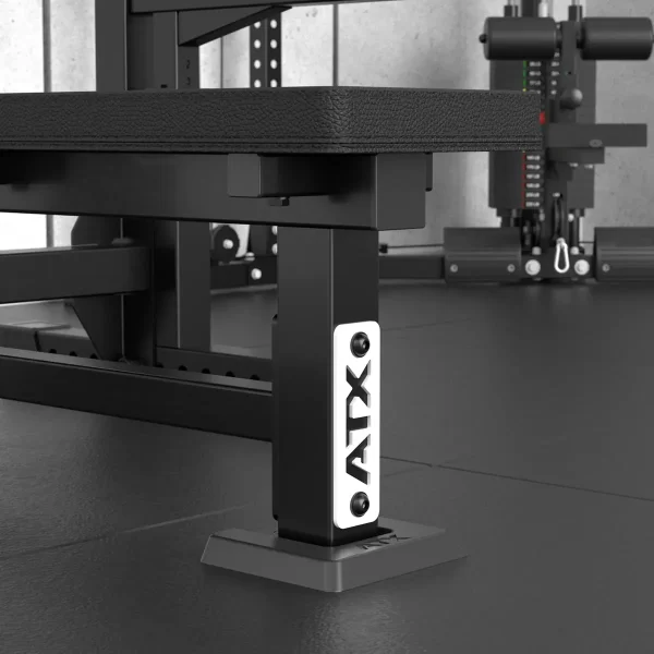 Close-up of the ATX® Olympic Bench Press 700 leg featuring the logo on a metal plate in a modern gym, surrounded by exercise equipment on black rubber mats.