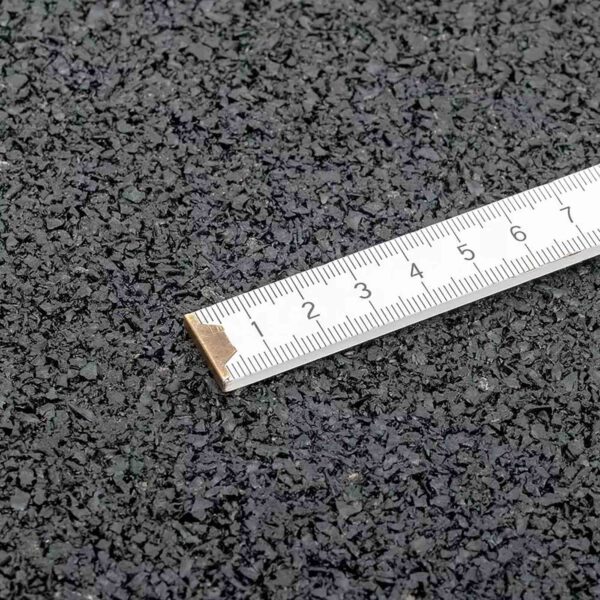 A close-up image of a ruler on the GymFloor RTS 50x50@20mm System, a textured black granular surface, shows measurements in centimeters with the starting edge aligned to the uneven texture.