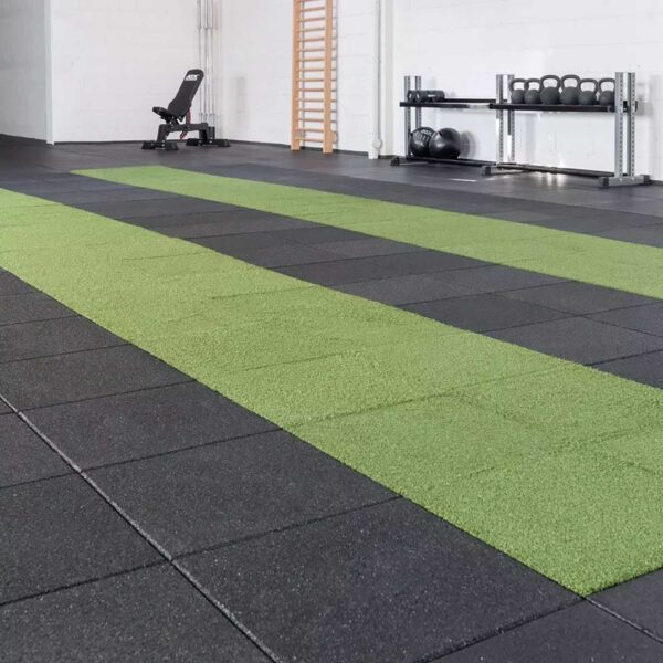 A gym features black flooring (GymFloor RTS 50x50@20mm System) with two green turf strips. A bench, wooden exercise ladder, and a rack holding kettlebells and medicine balls are visible in the open, well-lit space.
