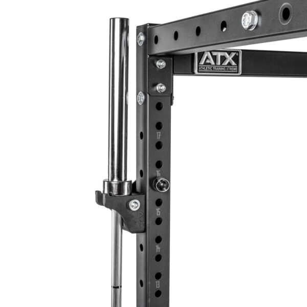 Close-up of the ATX® Bar Holder, a black metal squat rack featuring multiple holes and a chrome barbell. The ATX Athletic Training Xtreme logo is visible, with a secured clip holding the barbell in place.