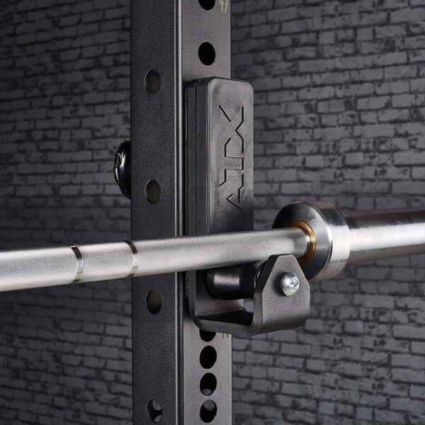 Close-up of an ATX® Roller J-Hooks Universal barbell on a black rack with adjustable holes and ATX branding, set against a textured gray brick wall.