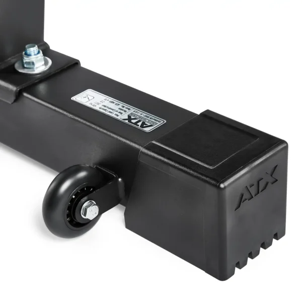 Close-up of a black metal structure resembling part of a folding fitness bench, featuring a caster wheel attached. The structure has a square end cap embossed with ATX, and bears a visible label. The wheel is mounted securely on a small axle with a nut.