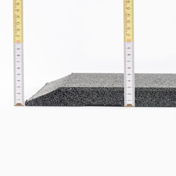The Shock & Sound Tile 30mm System, a black textured rubber mat, is displayed with two measuring tapes on the sides. The mat slopes upward from left to right, and the measuring tapes show the height of its edges against a plain white background.