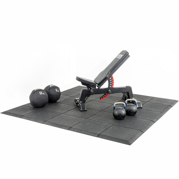 A home gym setup with an adjustable workout bench on a Shock & Sound Tile 30mm System mat. Two wall balls rest beside the bench, and two kettlebells are near the legs. The scene is minimalistic with a white background.