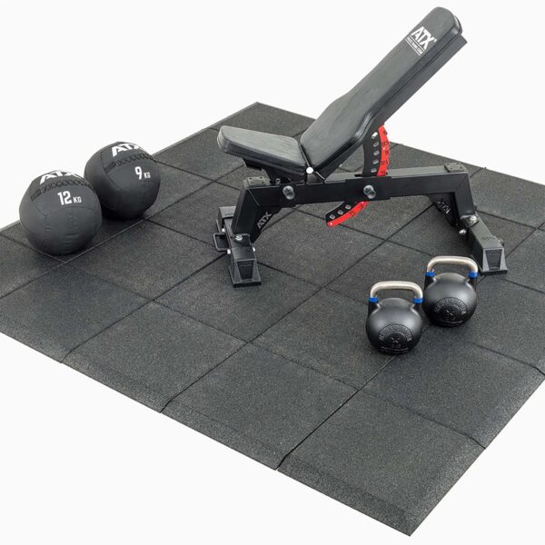 A gym setup with an adjustable black bench on Shock & Sound Tile 30mm System flooring, along with two kettlebells and two weighted medicine balls.