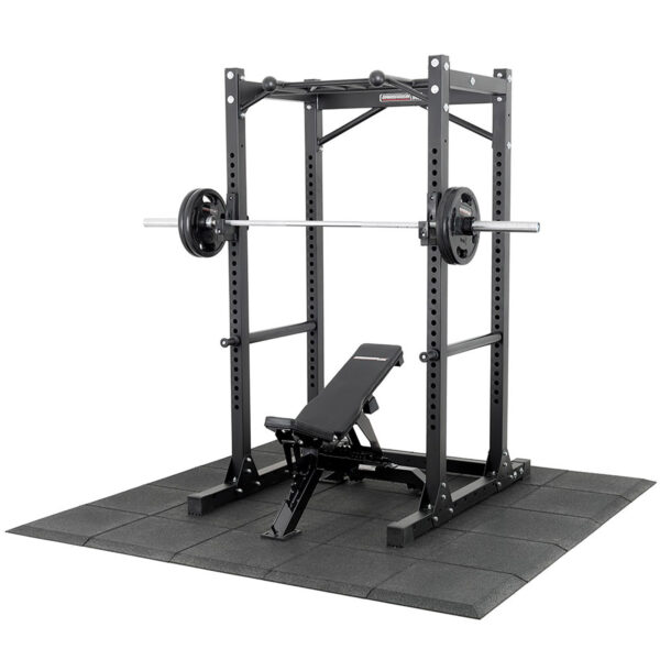 The Shock & Sound Tile 30mm System supports a power rack loaded with a barbell and weights on its black rubber mat, with an adjustable bench inside the rack for versatile strength training exercises.