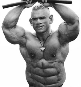 A black and white image of a muscular man with exaggerated features, including large ears and an intense expression, holding a bar above his head and wearing a Superman pendant.
