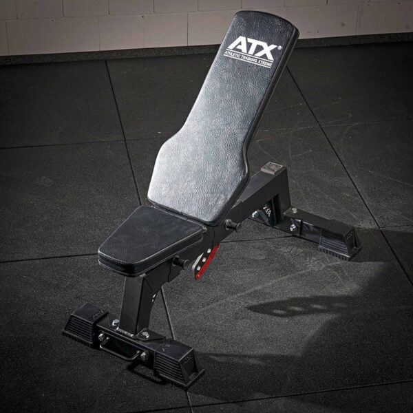 The ATX® Utility Bulls Bench, with a black padded seat and backrest, stands on a gym floor with dark rubber matting featuring a sturdy metal frame against a plain wall.