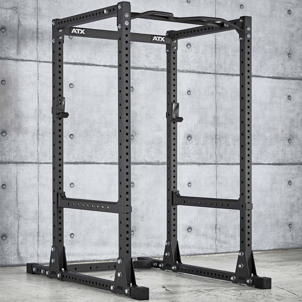 In a minimalist gym setting with a concrete wall backdrop, the ATX® Power Rack 770 XL SET stands out. This black rack features multiple adjustable holes for customizable workout setups, ideal for exercises such as squats and bench presses.