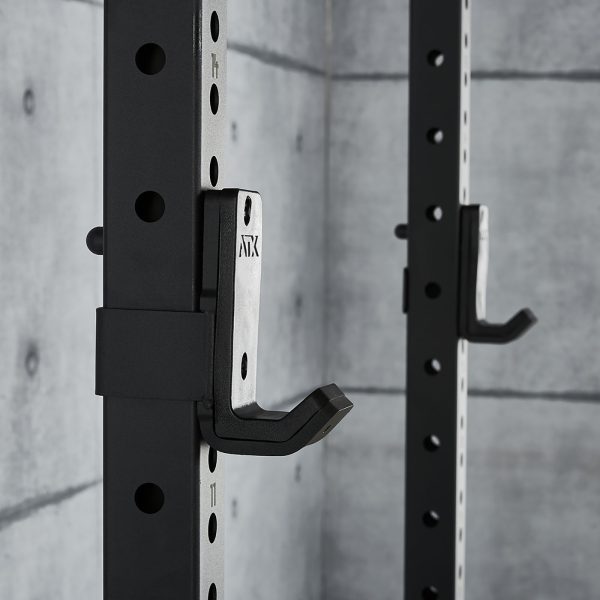 Close-up of the ATX® Power Rack 770 XL SET, a black steel squat rack with adjustable hooks. It features holes and numbering for height adjustments, set against a gray concrete wall in a modern minimalist gym.
