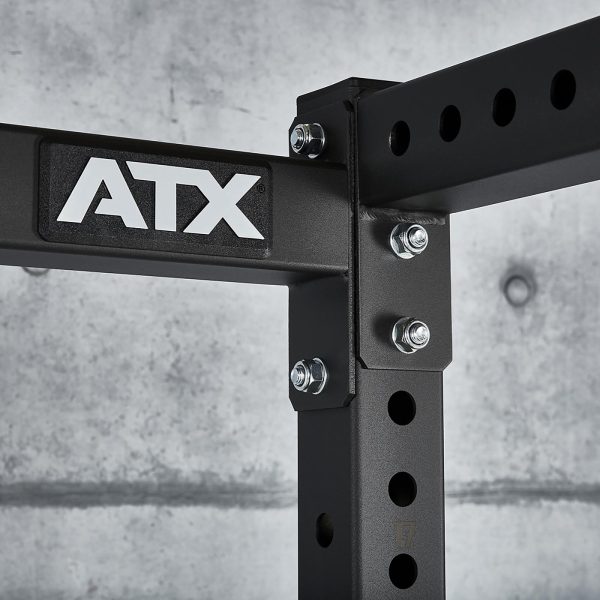 Close-up of the adjustable ATX® Power Rack 770 XL SET featuring multiple bolts and circular holes against a concrete wall. The name ATX appears on one of the horizontal bars.
