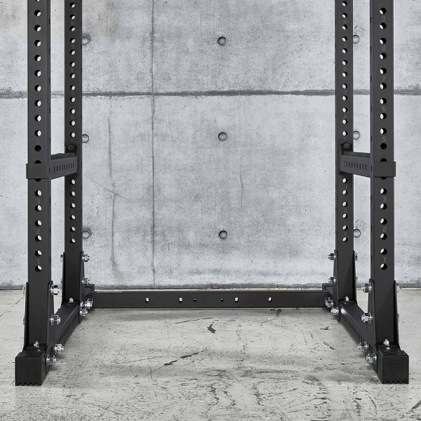 An ATX® Power Rack 770 XL SET made of black metal sits on a concrete floor against a concrete wall, featuring multiple holes for adjustable attachments, creating an industrial and minimalistic look.