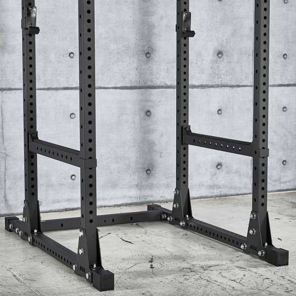 The ATX® Power Rack 770 XL SET, a black metal squat rack with adjustable height, stands on a concrete floor against a gray textured wall. It features numerous holes for customization and sturdy support beams at the base.