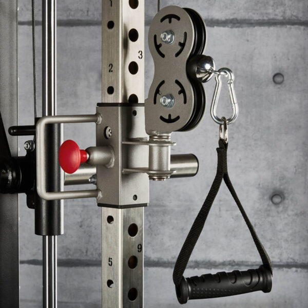 Close-up of the ATX® ERGO Stirrup Handle attached with a carabiner to a cable machine in the gym. A concrete wall is visible in the background, and weight adjustment numbers are marked on the equipment.