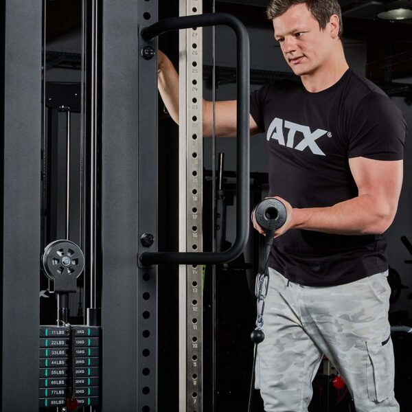 A man in an ATX tee adjusts a gym cable machine, holding a bar enhanced with ATX® Conic Fat Grips. The machine shows weight options starting at 11 lbs as he focuses on his setup.
