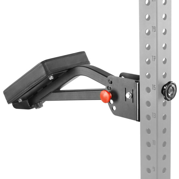 The ATX® The Bridge Supporting Pad, a black padded adjustable exercise bench attachment, is securely clamped onto a perforated metal gym rack with multiple numbered holes for positioning, featuring a visible red knob for secure attachment.