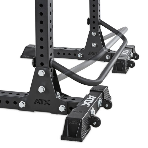 Close-up of a black ATX® Squat Stands Brace with adjustable safety arms. The rack features customizable holes and large bolts for stability, with foot caps securing the base. A partially blurred safety bar shows movement.