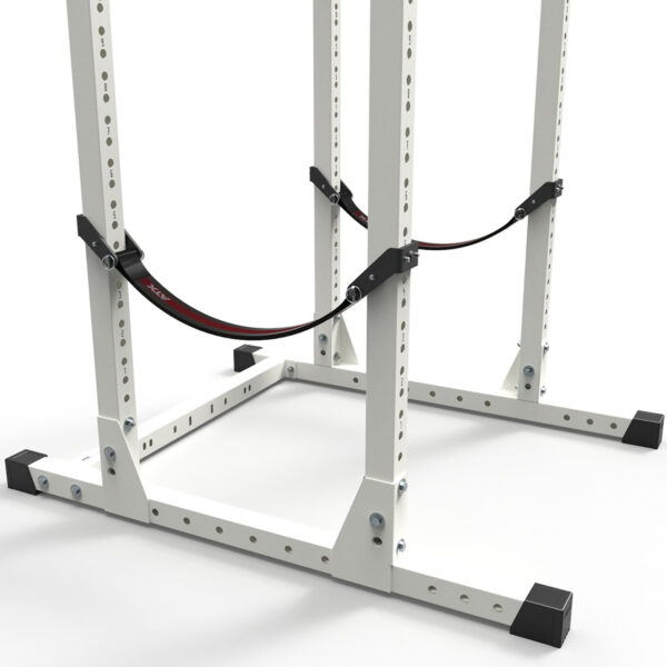 A close-up shows a gym squat rack featuring the ATX® Safety Strap 700 70cm for added security. The white rack with black accents is set on a plain gray floor, with safety straps securely attached to its structure.