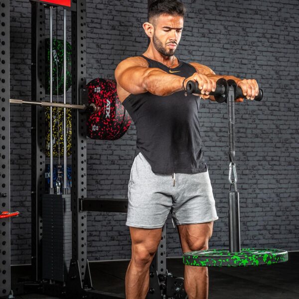 A man in a gym, wearing a black tank top and gray shorts, exercises intensely with the ATX® Forearm Training Set bar, weight plates attached. Gym equipment and a textured brick wall form the background.