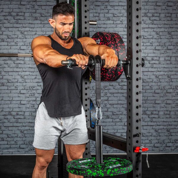 Wearing a black sleeveless shirt and gray shorts, an individual exercises in the gym with the ATX® Forearm Training Set. Positioned in front of a power rack, they grip handles linked to weights, while brick walls and exercise equipment can be seen in the background.