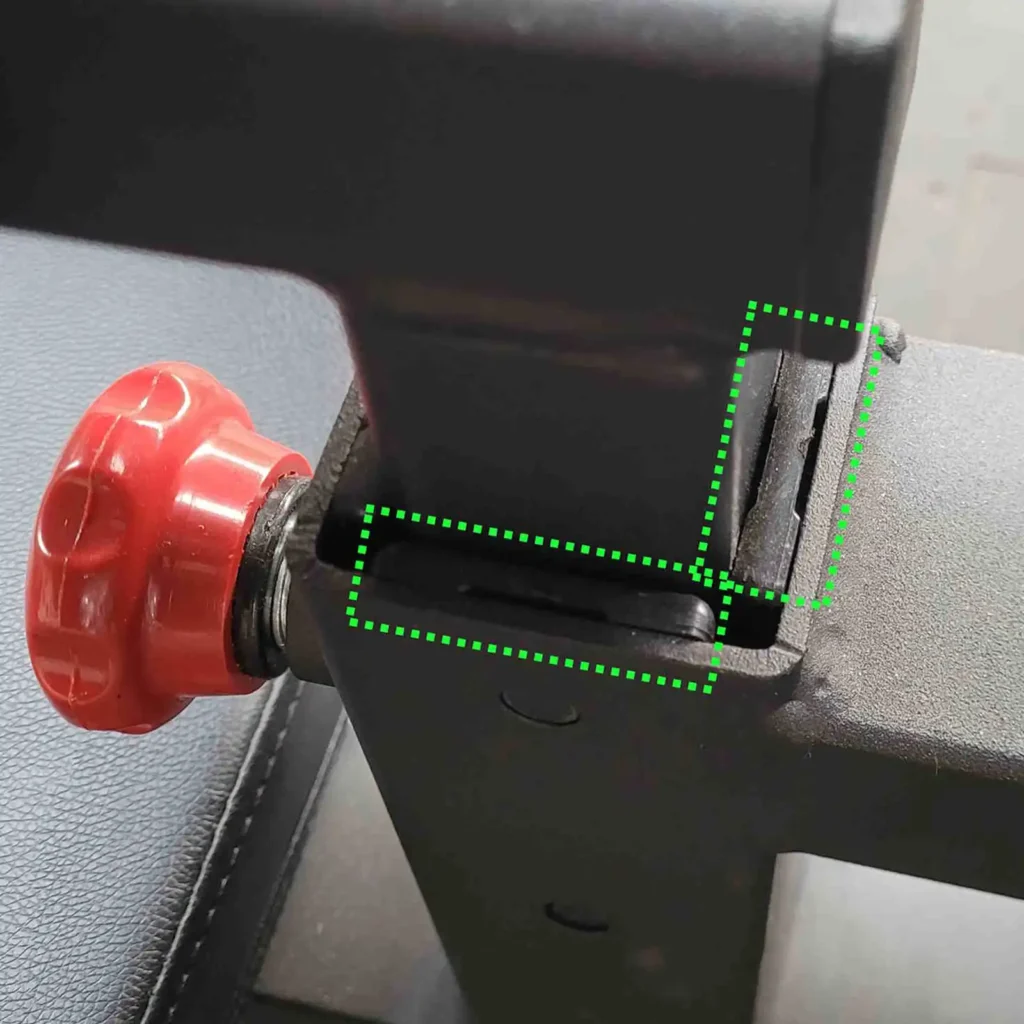 Close-up of a lat pulldown and row machine joint, highlighting a crack with green dotted lines. A red adjustment knob is visible on the left, next to the joint. The background is a textured surface.