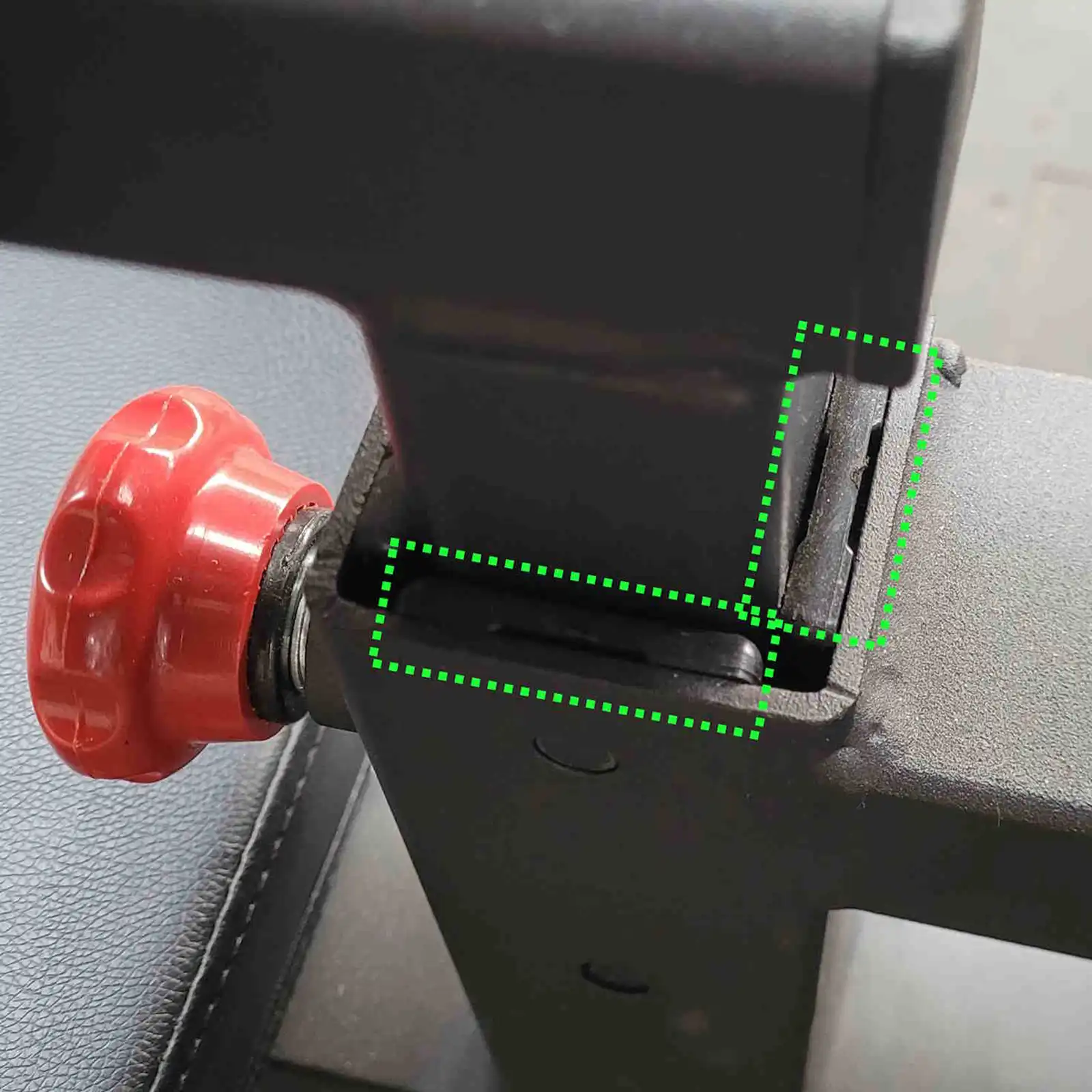 Close-up of a lat pulldown and row machine joint, highlighting a crack with green dotted lines. A red adjustment knob is visible on the left, next to the joint. The background is a textured surface.