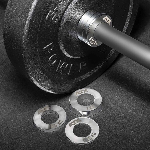 A close-up shows a black barbell weight plate labeled POWER 1 KG with three smaller silver plates nearby, branded ATX and marked 0.25 kg, 0.5 kg, and 1 kg, from the ATX® Olympic Fractional Plate Pairs collection on a dark surface.