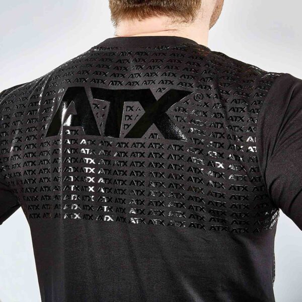 Rear view of a person wearing an ATX® Grip Shirt with black fabric and a shiny grid-like ATX logo pattern across the back, standing against a light gray background.