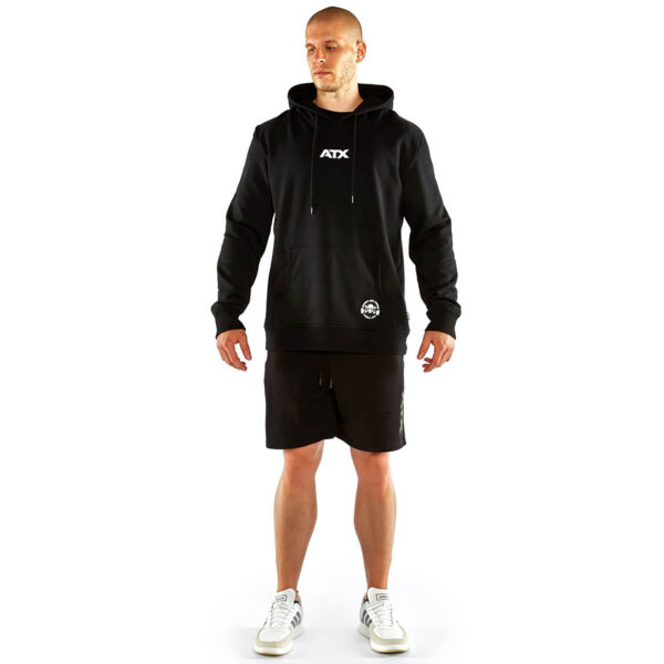 A person wearing an ATX® Black Hoodie, black shorts, and white sneakers stands against a white background with hands relaxed at their sides.