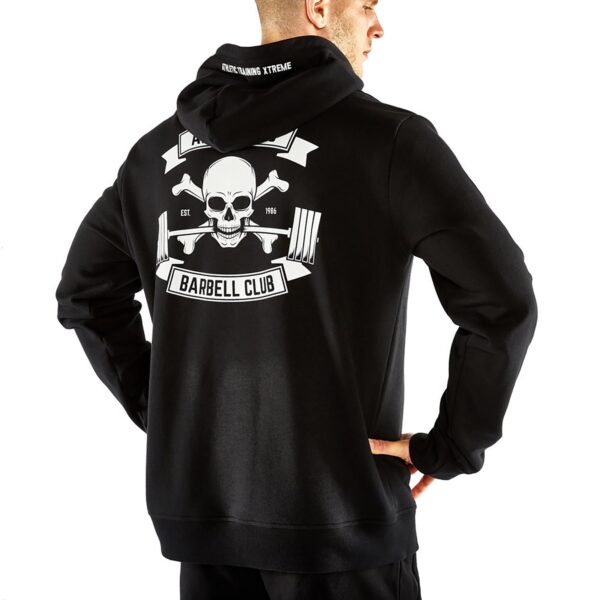 A person stands with hands on hips, wearing the ATX® Black Hoodie. The back design features a skull, crossed dumbbells, and text Barbell Club, while Overcoming Xtreme adorns the hood.
