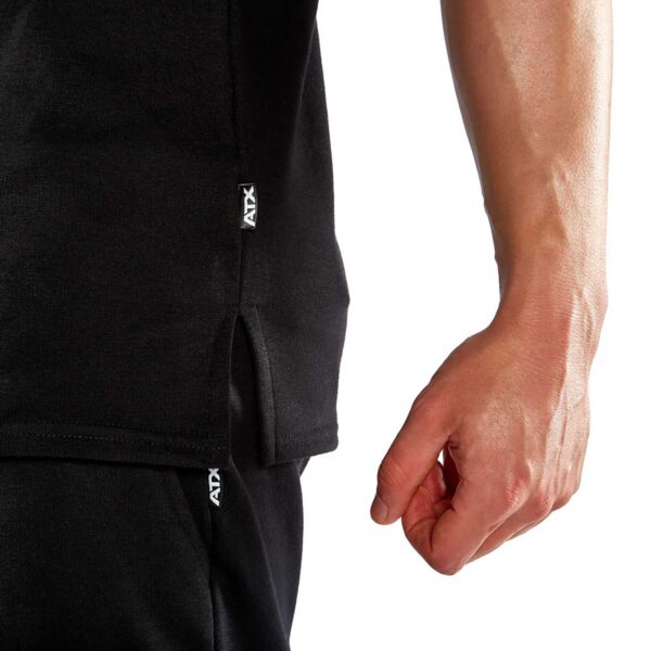 A close-up image shows a person’s right hand near their body, wearing the ATX® Muscle Shirt in black. The garment features a small, visible ATX label against a white background.