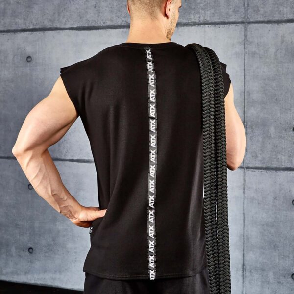 Wearing an ATX® Muscle Shirt, a person stands against a concrete wall, holding a coiled rope over their shoulder, showcasing the logo on the back.
