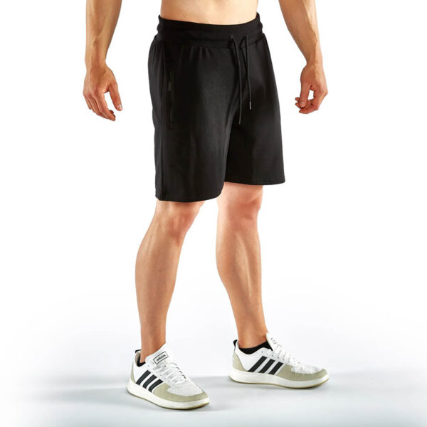Against a white background, a person is wearing black ATX® Black Shorts, a matching top, and white sneakers with black stripes. The image shows the individual from the neck down, highlighting their casual athletic outfit.