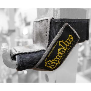Close-up of a Spud Inc 5R Barbell Shield, black and gray with Spud Inc. in yellow, looped on a metal rack with a hook. Blurred gym equipment in the background.